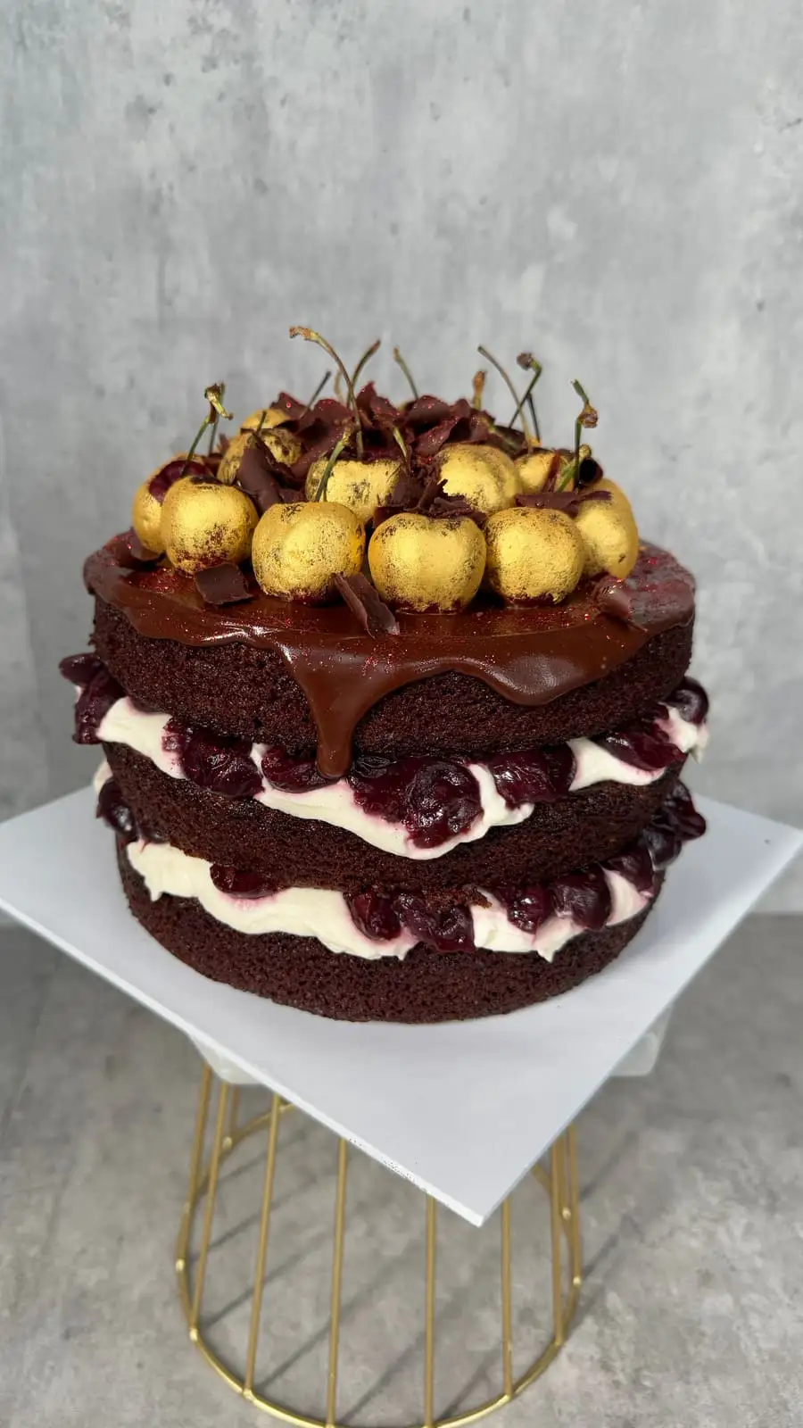 Three-layer chocolate cake filled with cream and cherry compote, topped with gold-dusted cherries.